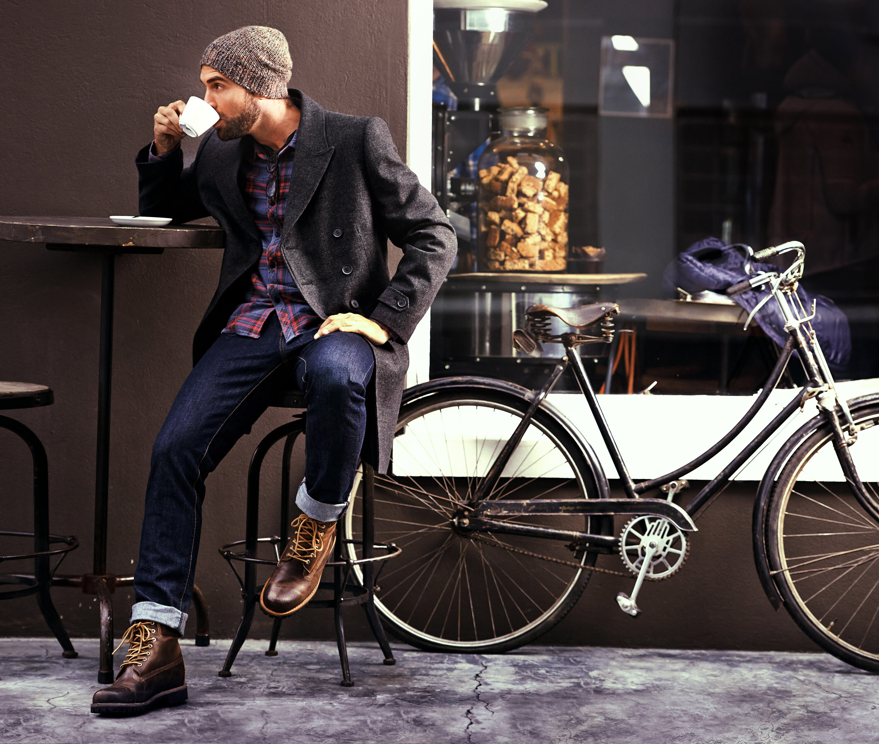 Shot of a handsome young man enjoying a cup of coffee at a cafe in the city while his bike stands next to him
